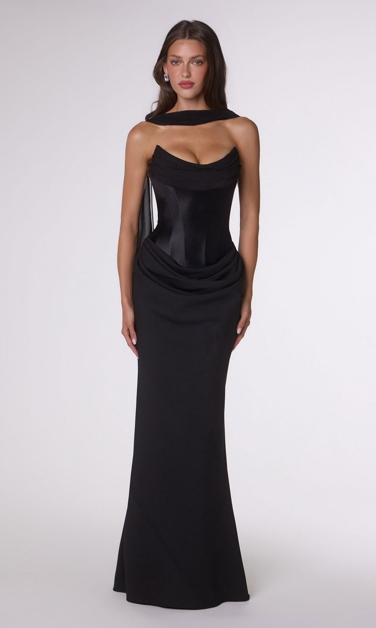 A woman stands against a plain background wearing the Amoris T732 long prom dress—a fitted black stretch satin gown featuring a draped bodice and structured corset back detailing.